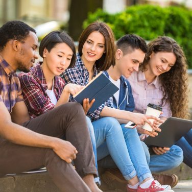 Group of young attractive smiling students dressed casual sitting on the staircase outdoors on campus at the university.